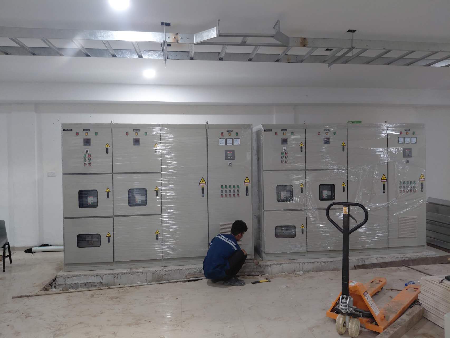 Teknisi bekerja pada panel switchboard yang baru diposisikan selama instalasi