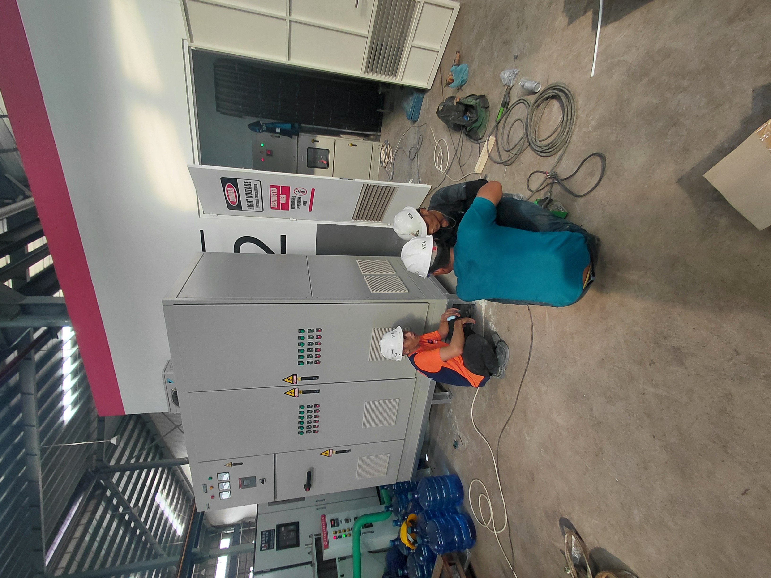 Teknisi bekerja di samping panel kontrol elektrikal industri