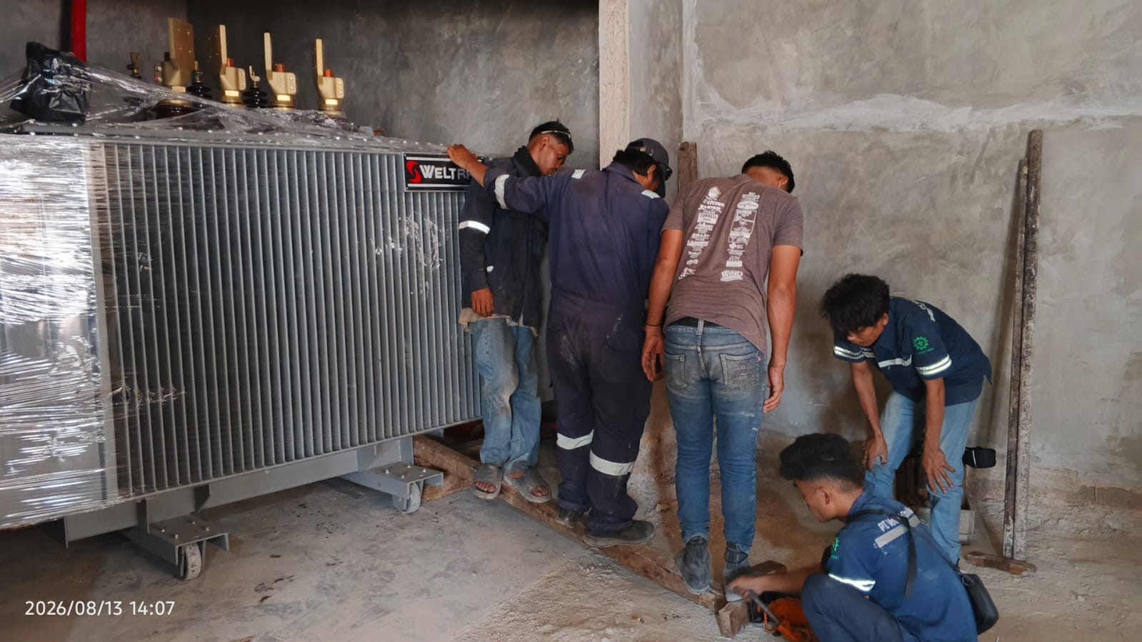 Tim teknisi memposisikan transformer besar di dalam ruang elektrikal